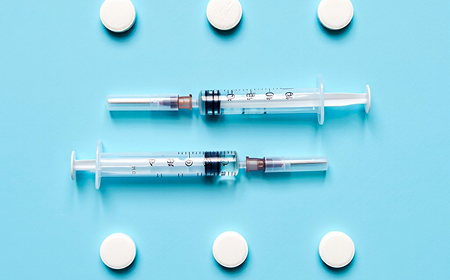 Два медицинских шприца и белые круглые таблетки на голубом фоне